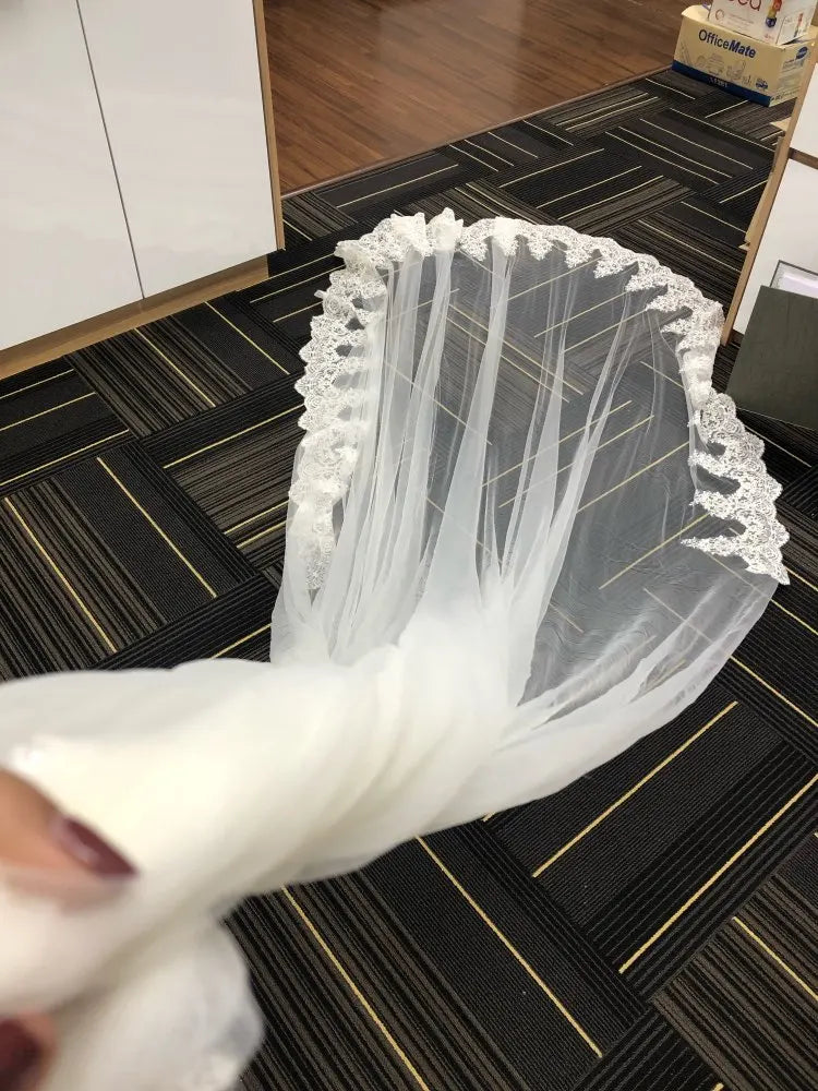 White wedding veil with lace details held by a hand on a black and gold patterned floor.