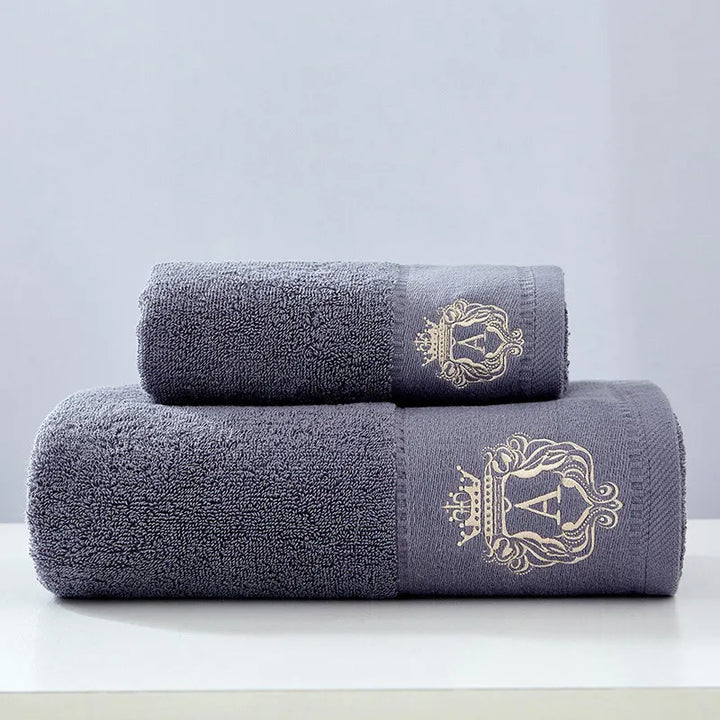 Dark gray cotton towel set with two stacked folded towels and gold crest embroidery.