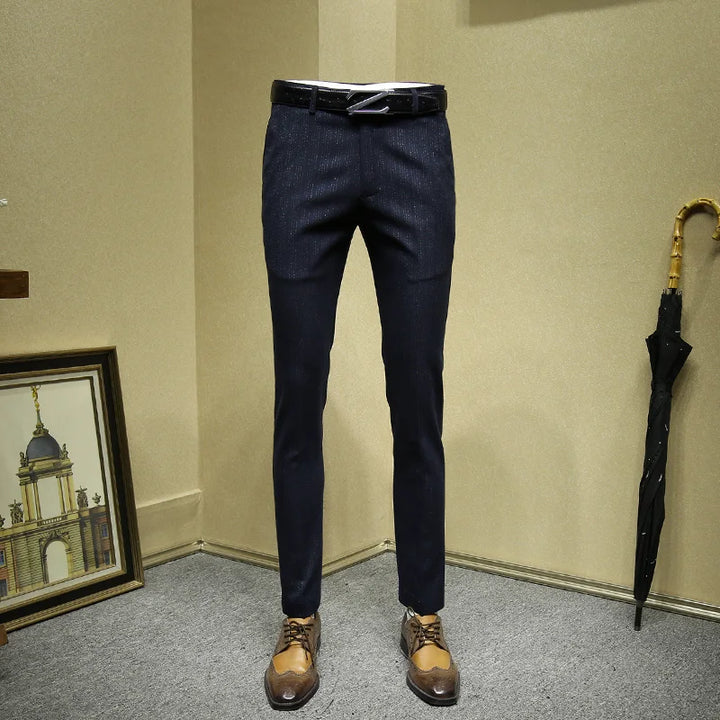 Dark blue pants displayed against a beige wall with a framed picture and umbrella in the background.