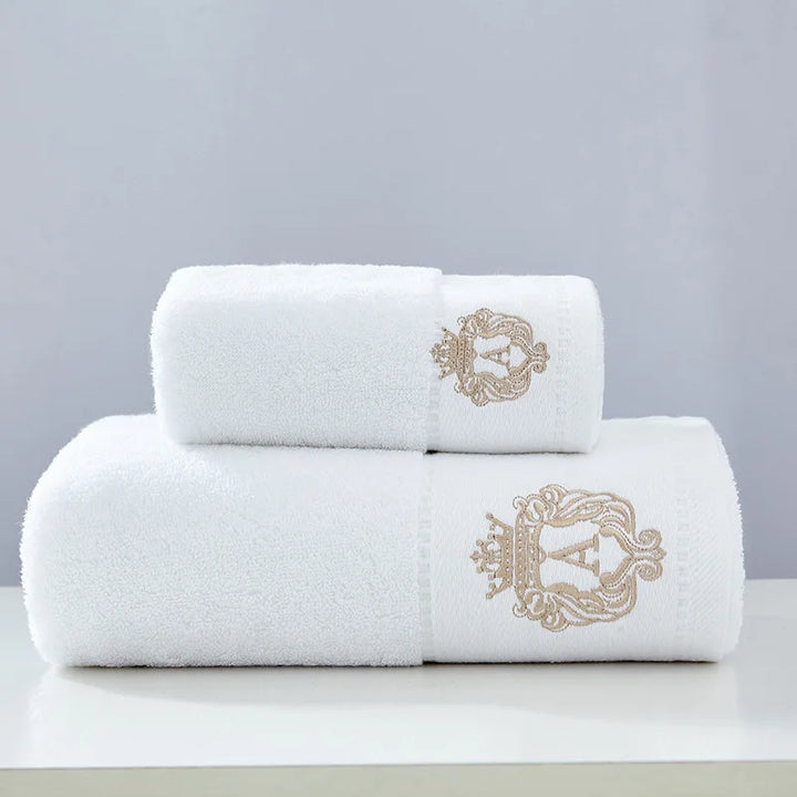 White cotton towel set with two folded towels and embroidered gold crest on the end panel.