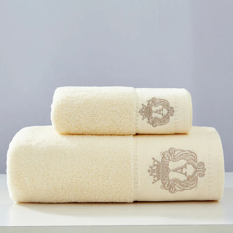 Cream cotton towel set with two stacked folded towels and embroidered gold crest details.