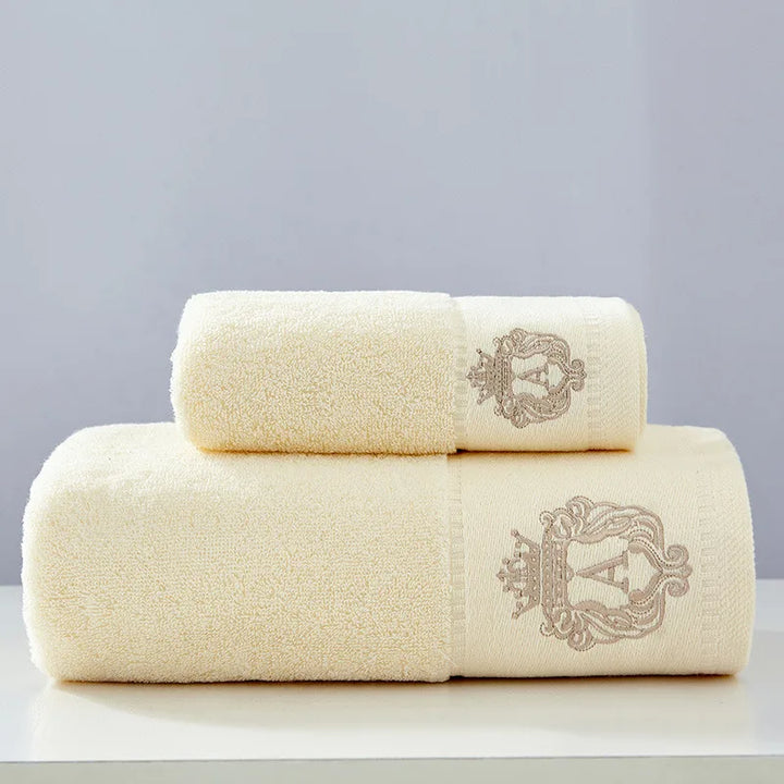 Cream cotton towel set with two stacked folded towels and embroidered gold crest details.