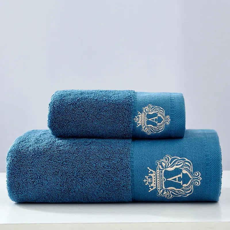 Blue cotton towel set with two folded towels and embroidered gold crest on the side.