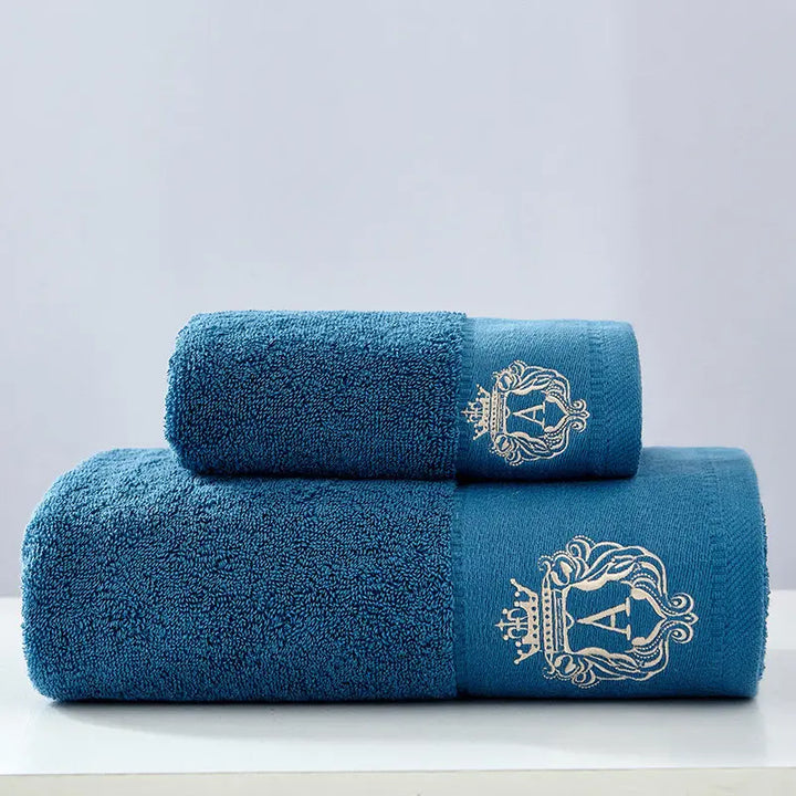 Blue cotton towel set with two folded towels and embroidered gold crest on the side.