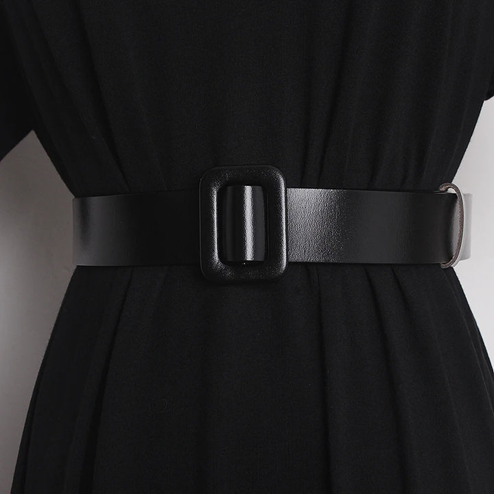 Narrow black leather belt on dress waist with rectangular buckle