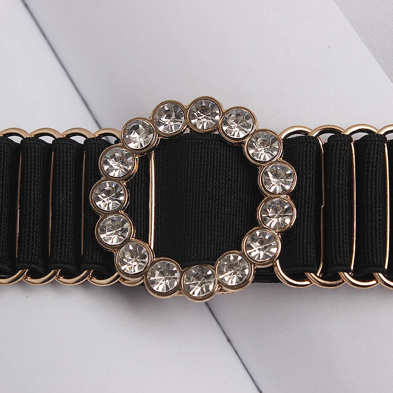 Black elastic belt close-up with circular rhinestone buckle and gold-tone metal links