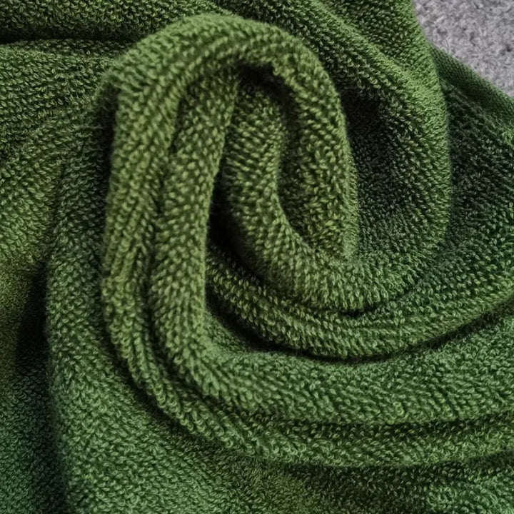 Rolled green cotton towel with soft terry texture and embroidered Greek key trim