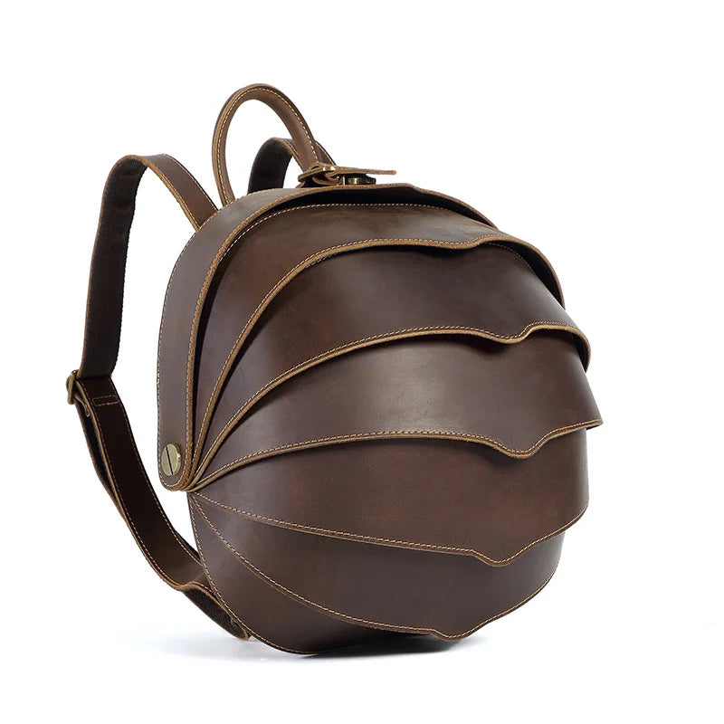 Brown leather round backpack with curved flap, top handle, and adjustable shoulder strap.