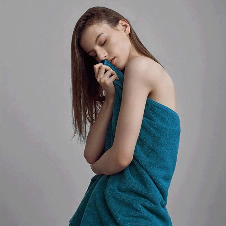 Person wrapped in a teal-blue cotton bath towel with embroidered crest