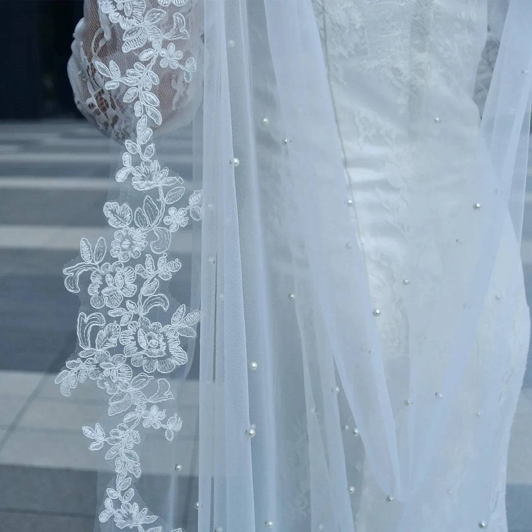 Close-up of white sheer bridal cape with floral lace applique and pearl-like bead dots