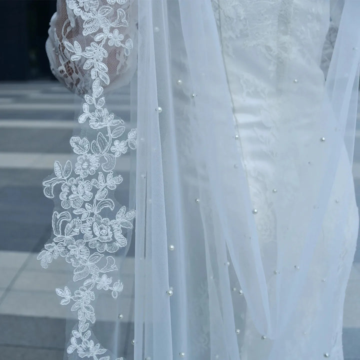 Close-up of white sheer bridal cape with floral lace applique and pearl-like bead dots