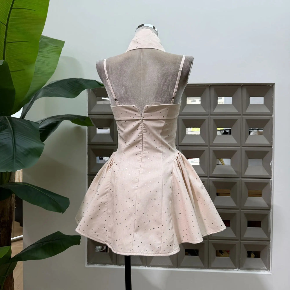 Back view of beige polka dot mini dress with open back and bow waist detail