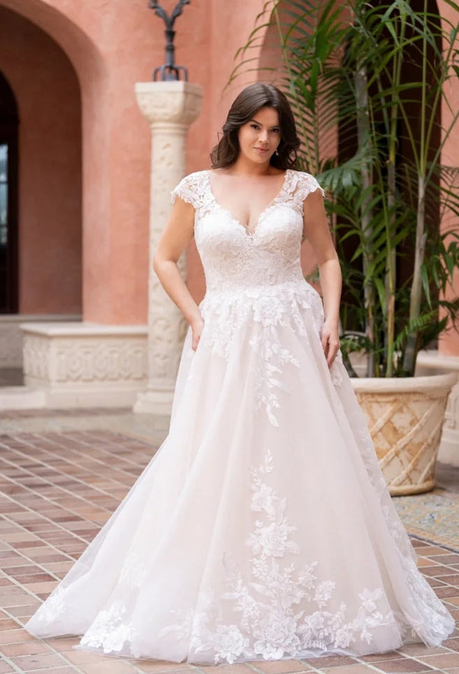 Woman in a white lace wedding dress standing in front of a pink building with plants.