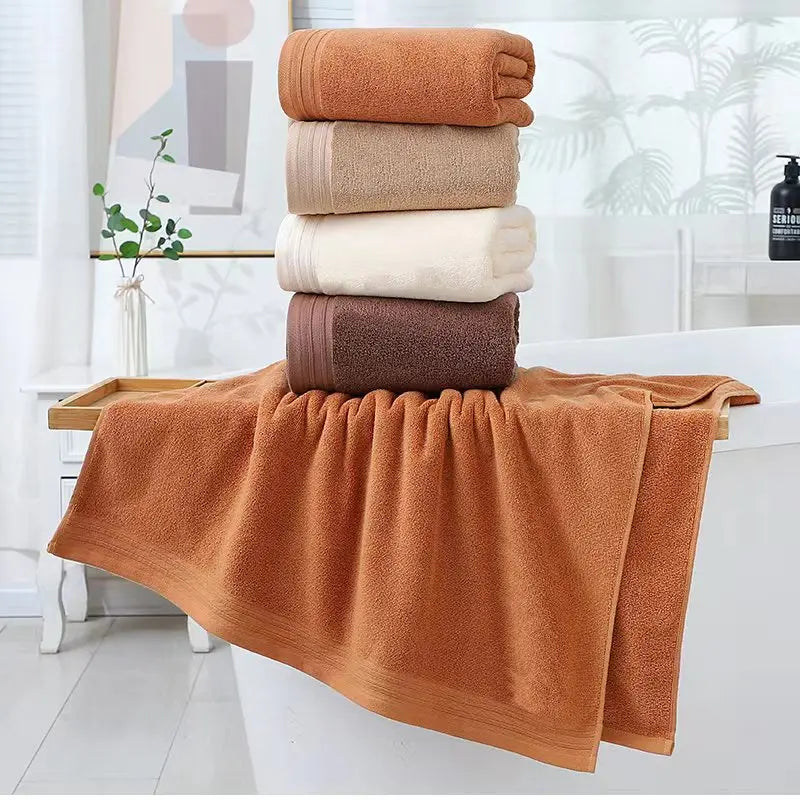Stacked solid cotton towels in terracotta, cream, and brown with one towel draped