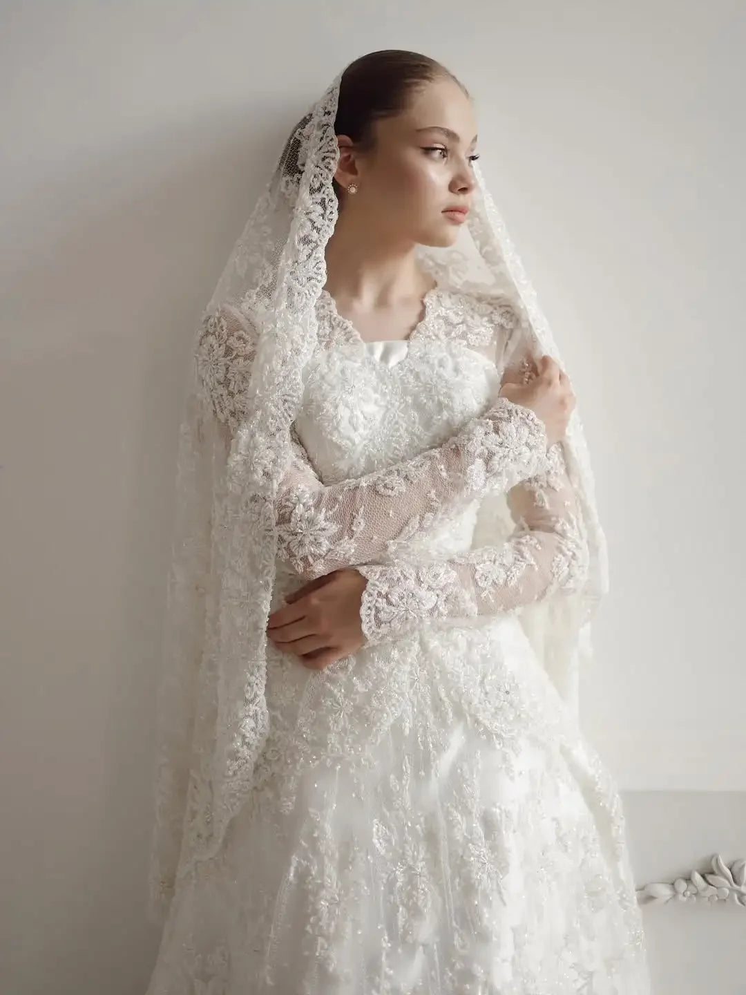Ivory lace A-line wedding dress with high neckline, long illusion sleeves, and floral details.