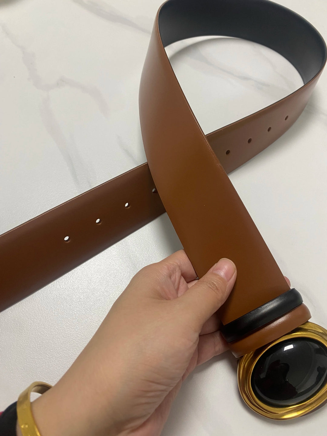 Wide leather belt in tan-brown with oval black center buckle and multiple adjustment holes