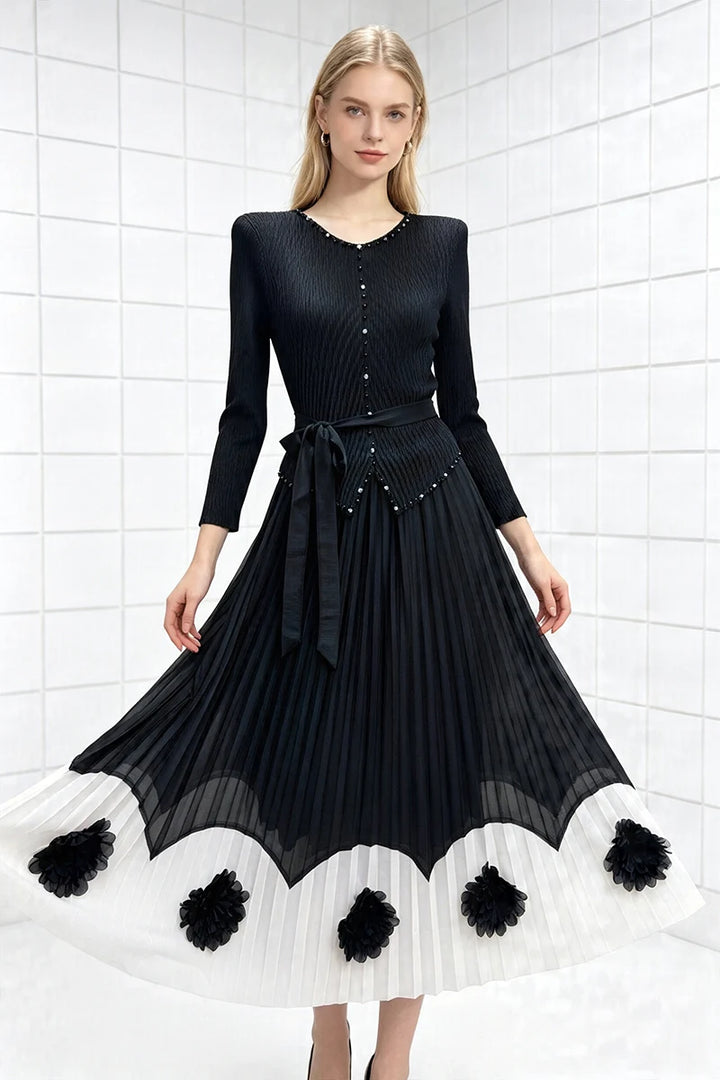 Black pleated midi party dress with long sleeves, tie waist, scalloped pom hem and floral accents.