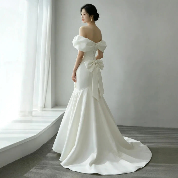 White satin off-shoulder wedding ball gown with soft puff sleeves and tied bow