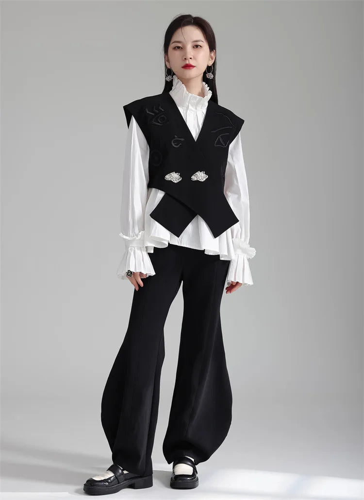 Black irregular women’s suit waistcoat with V-neck and silver buttons over white blouse.