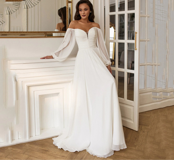 Woman in a white wedding dress standing in a room with wooden floor and white walls.