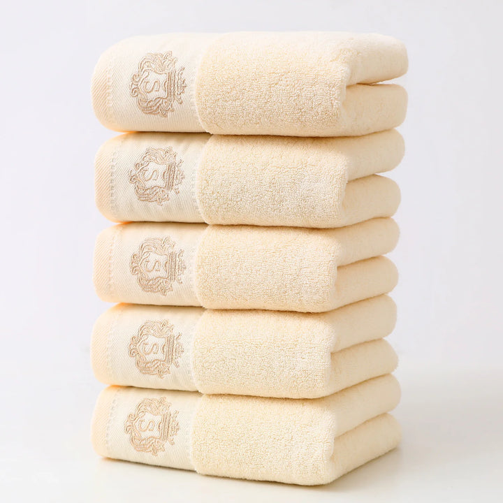 Beige 5-piece bathroom towel set with gold embroidered monograms, folded stack