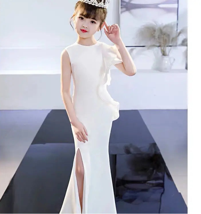 Woman in a white evening gown with a high slit, standing indoors.