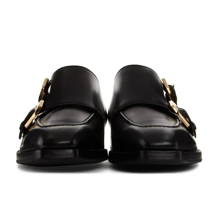 Black loafers with gold buckles on a white background, branded 'Stiglitz'.
