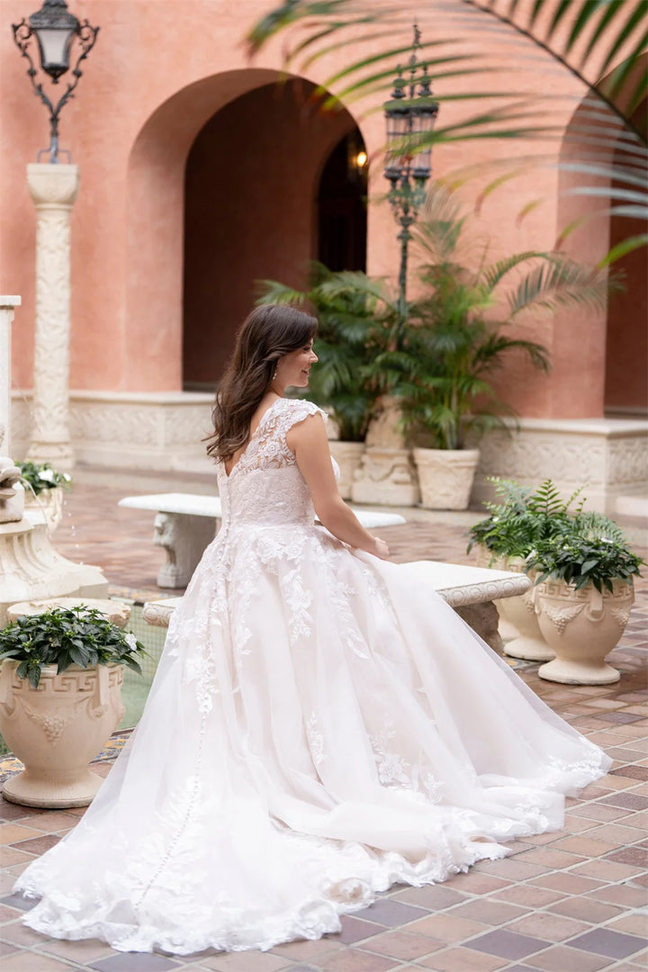 Woman in a white wedding dress standing in an outdoor setting with plants and arches.