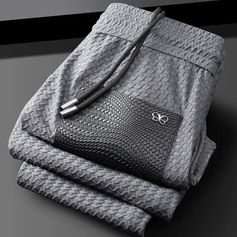 Grey woven slim-fit trousers with textured pattern and bow emblem on pocket