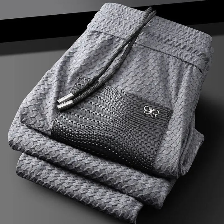 Grey woven slim-fit trousers with textured pattern and bow emblem on pocket