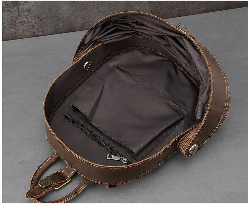 Dark brown leather backpack open to interior with zip pocket and compartments.