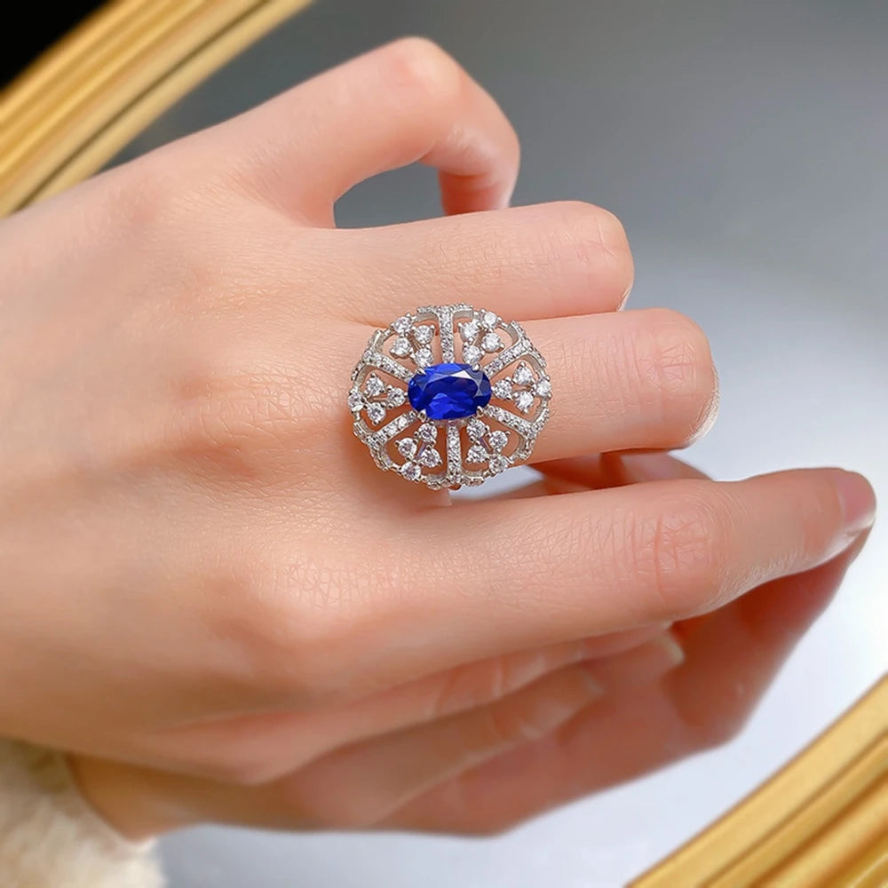 Silver ring on hand: blue oval center stone with halo of clear stones and prongs