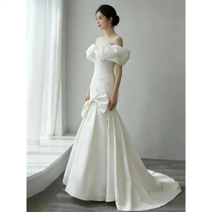 White off-shoulder satin wedding gown with draped fitted bodice and flowing A-line skirt