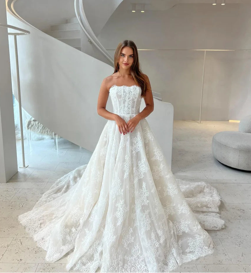 Woman in a white lace wedding dress standing in a modern indoor setting.