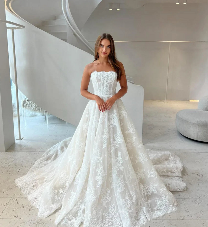 Woman in a white lace wedding dress standing in a modern indoor setting.