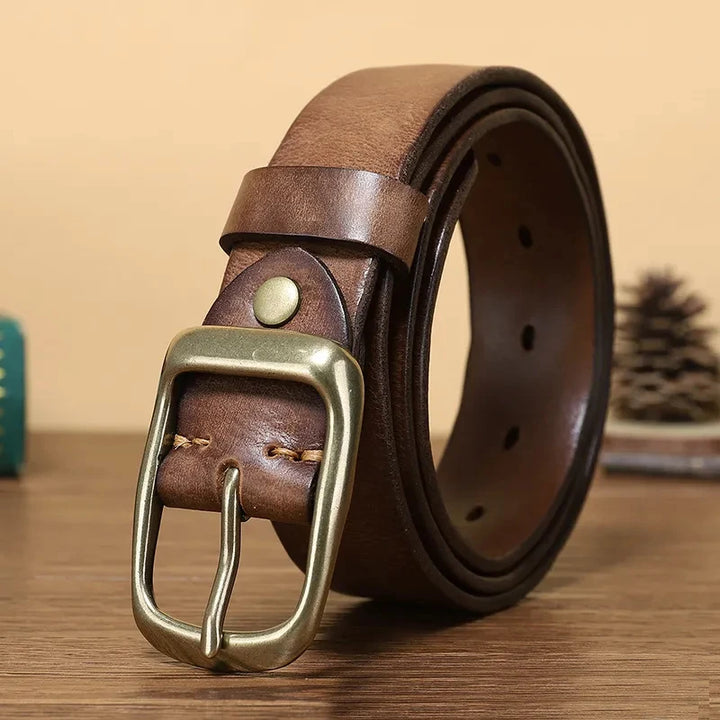 A brown genuine leather belt with a vintage copper buckle, resting on a wooden surface.