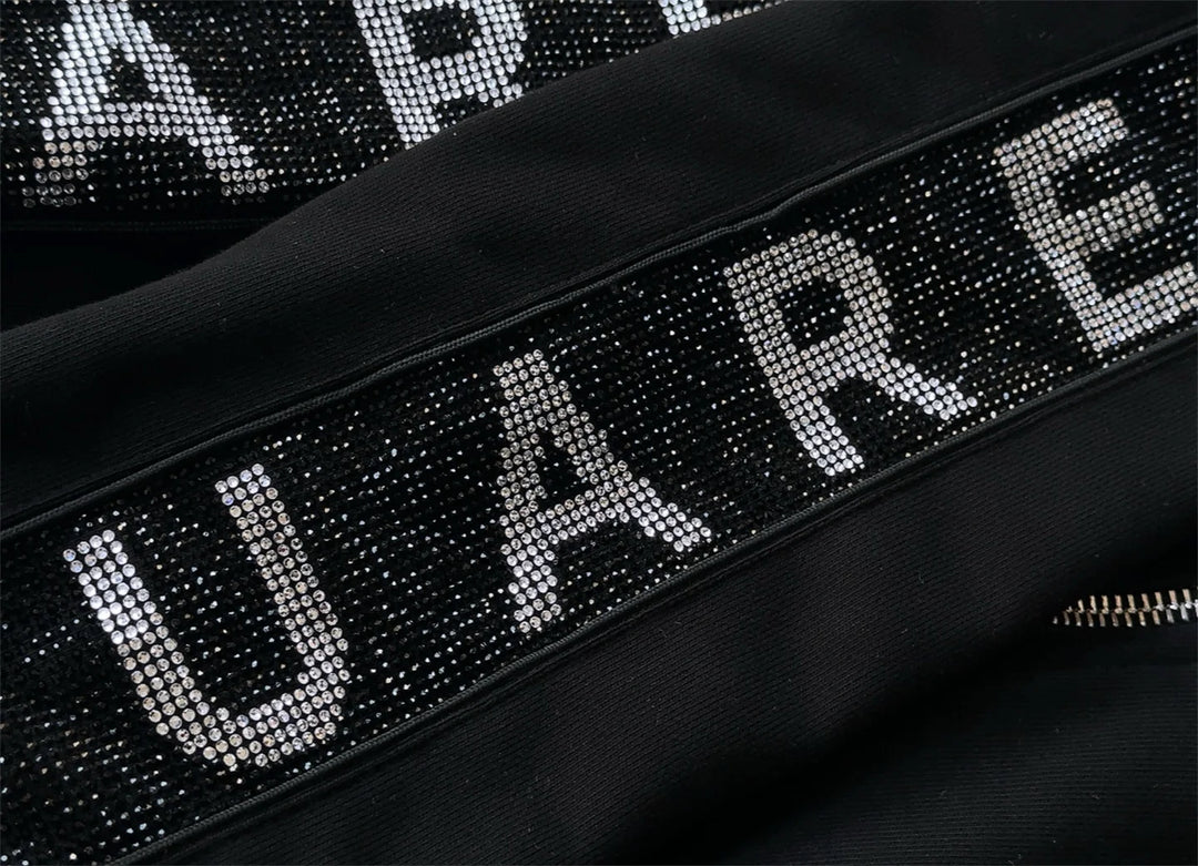 Black tracksuit jacket detail: rhinestone letter band with front zipper
