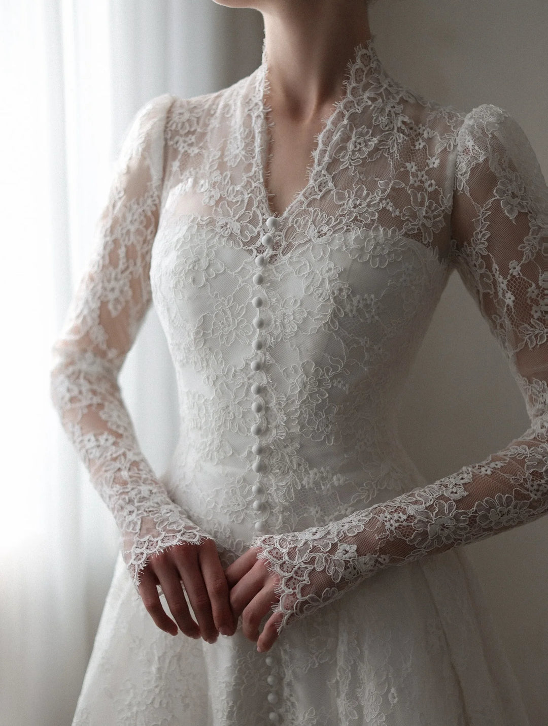 White lace bridal gown close-up: V-neck, button-front detail, and long sleeve lace