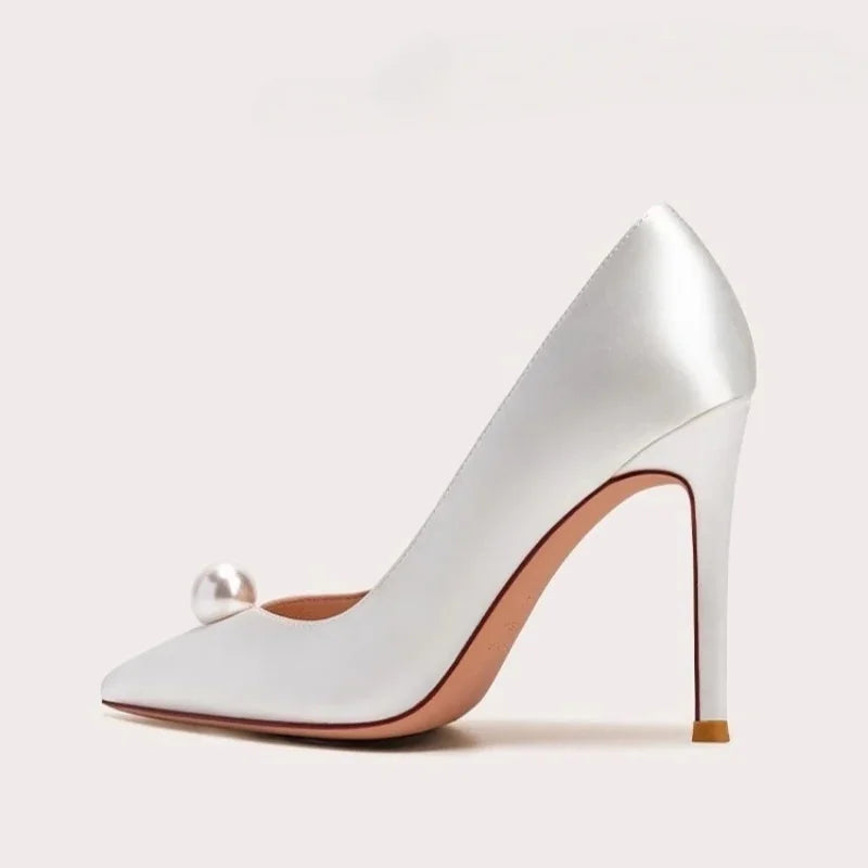White satin slip-on pumps with pearl ornament, pointed toe, and gold stiletto heel