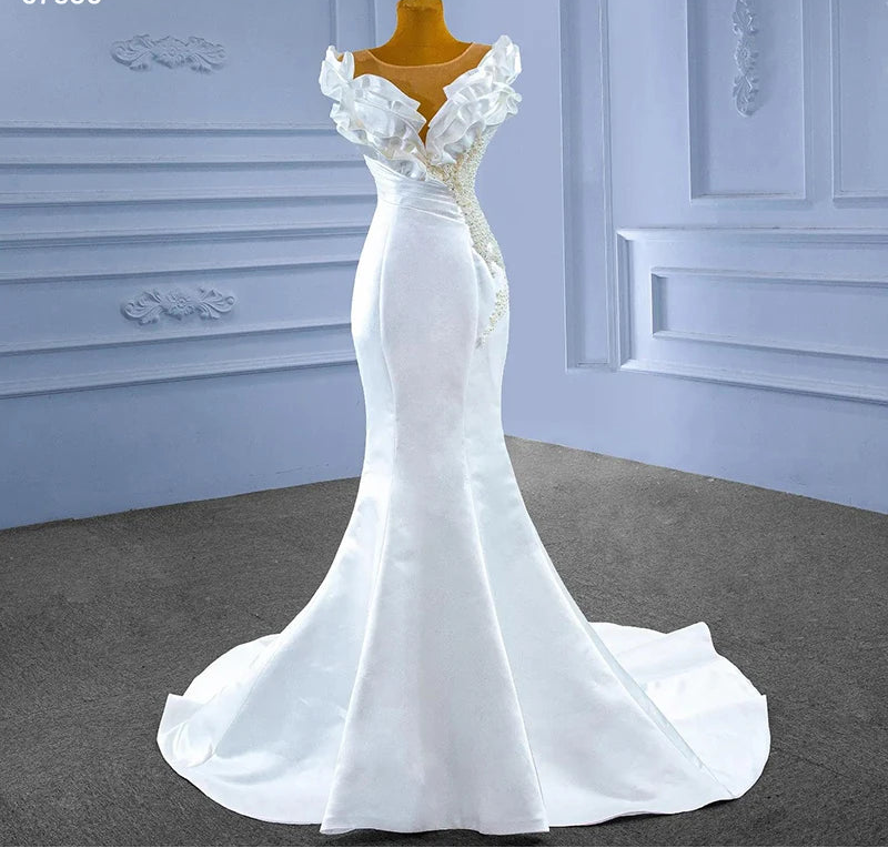 White evening gown on a mannequin against a decorative wall.