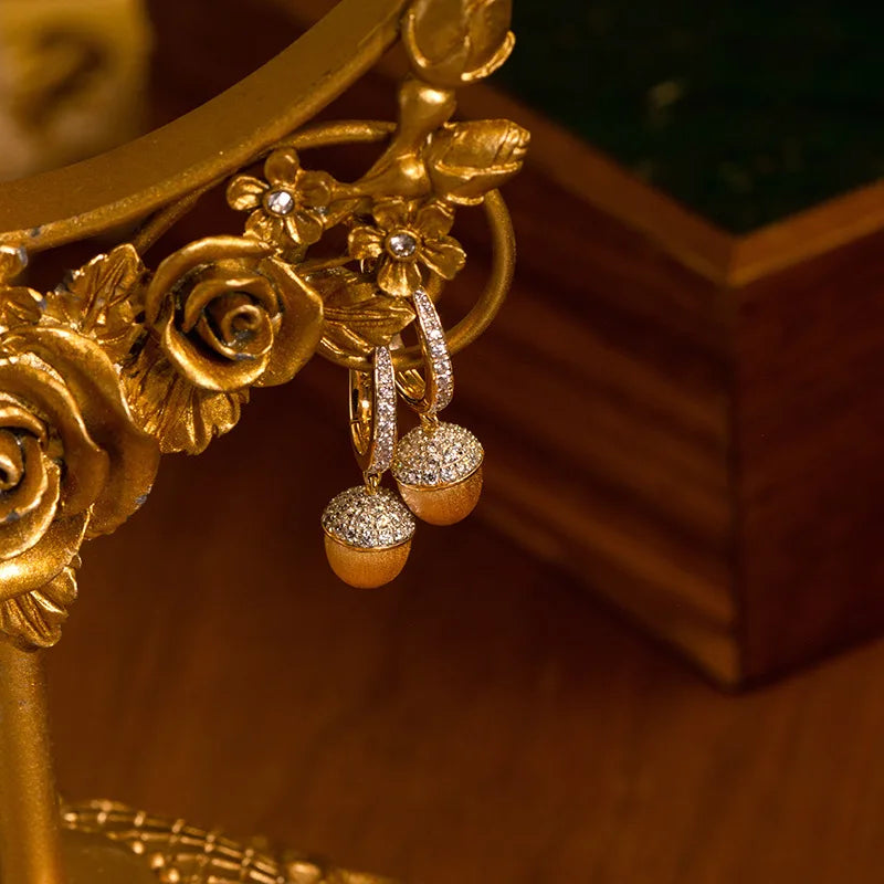 Gold earrings with acorn design on a decorative stand