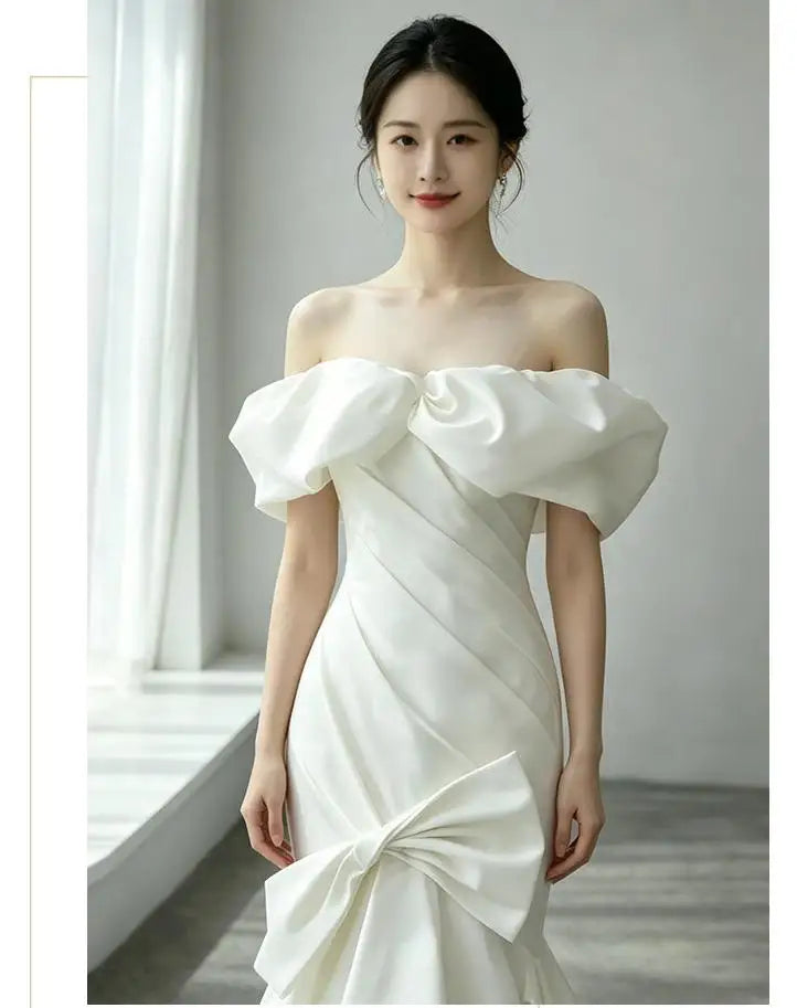 White off-shoulder satin wedding gown with sculpted drape bodice and bow accent at waist