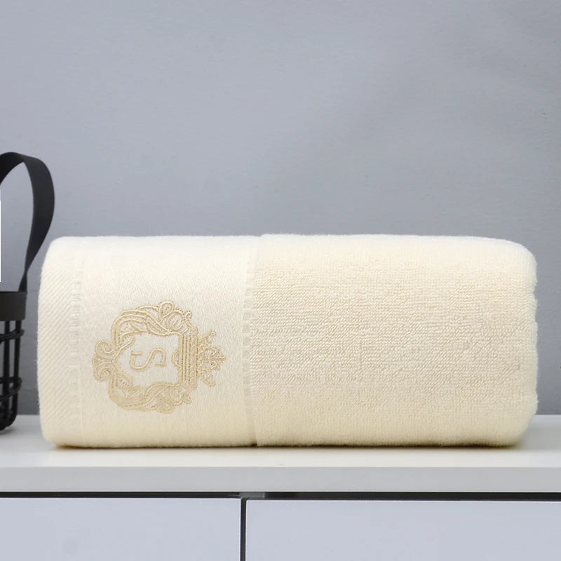 Cream cotton bathroom towel with embroidered emblem, folded and neatly rolled