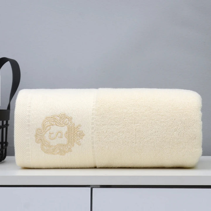 Cream cotton bathroom towel with embroidered emblem, folded and neatly rolled