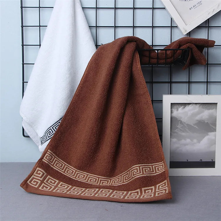 Cotton bathroom towel set in rust-brown with woven Greek border, folded.