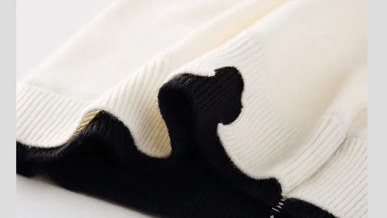 Off-white pullover sweater fabric close-up with fine knit texture and black cuff trim.