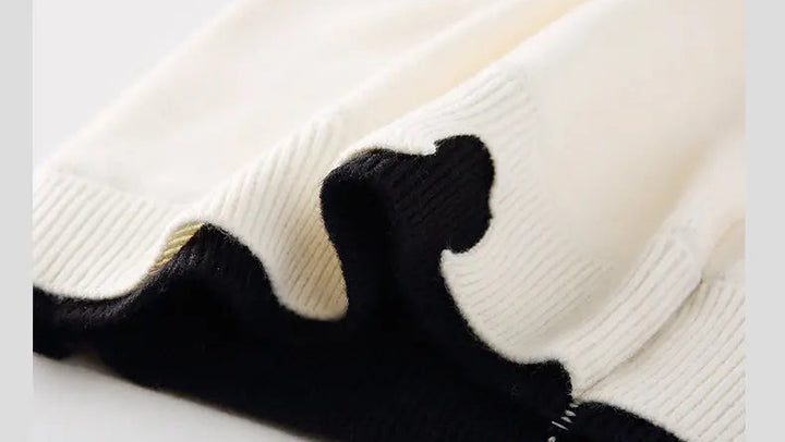 Off-white pullover sweater fabric close-up with fine knit texture and black cuff trim.