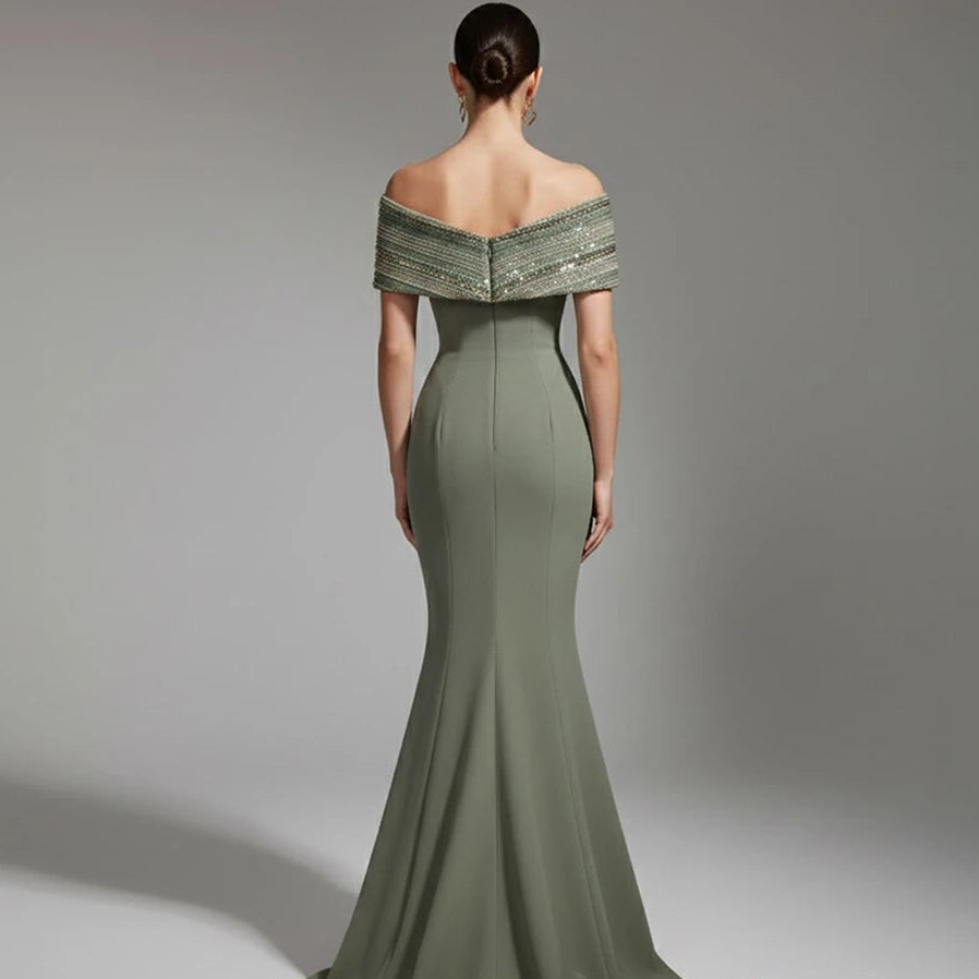 Woman wearing a green off-shoulder evening gown with intricate detailing on a gray background.