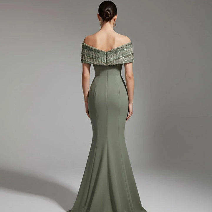 Woman wearing a green off-shoulder evening gown with intricate detailing on a gray background.