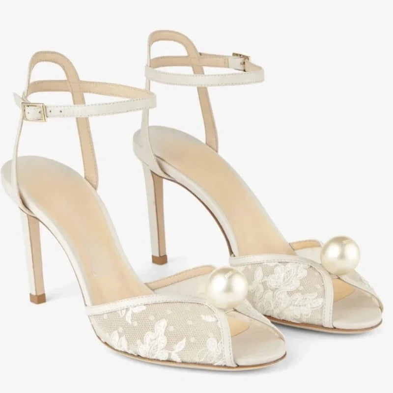 Pair of white strappy high heels with lace panels, stiletto heel, and pearl buttons